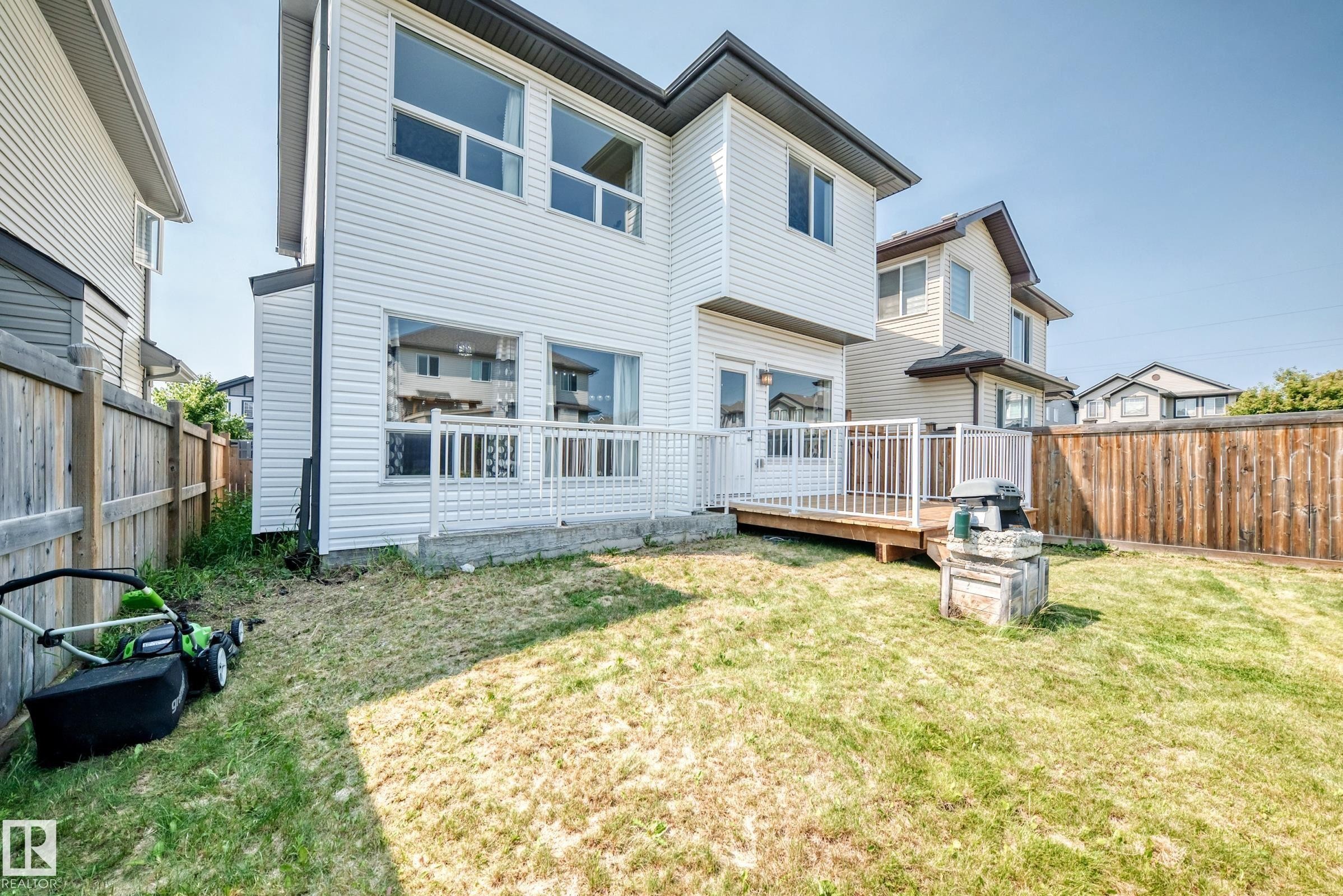 Spacious backyard featuring a level lawn with mature landscaping, wooden privacy fencing, and a multi-level deck with white railings - 2923 16 Street Nw, Edmonton, AB - Outdoor With Deck Patio Veranda With Exterior