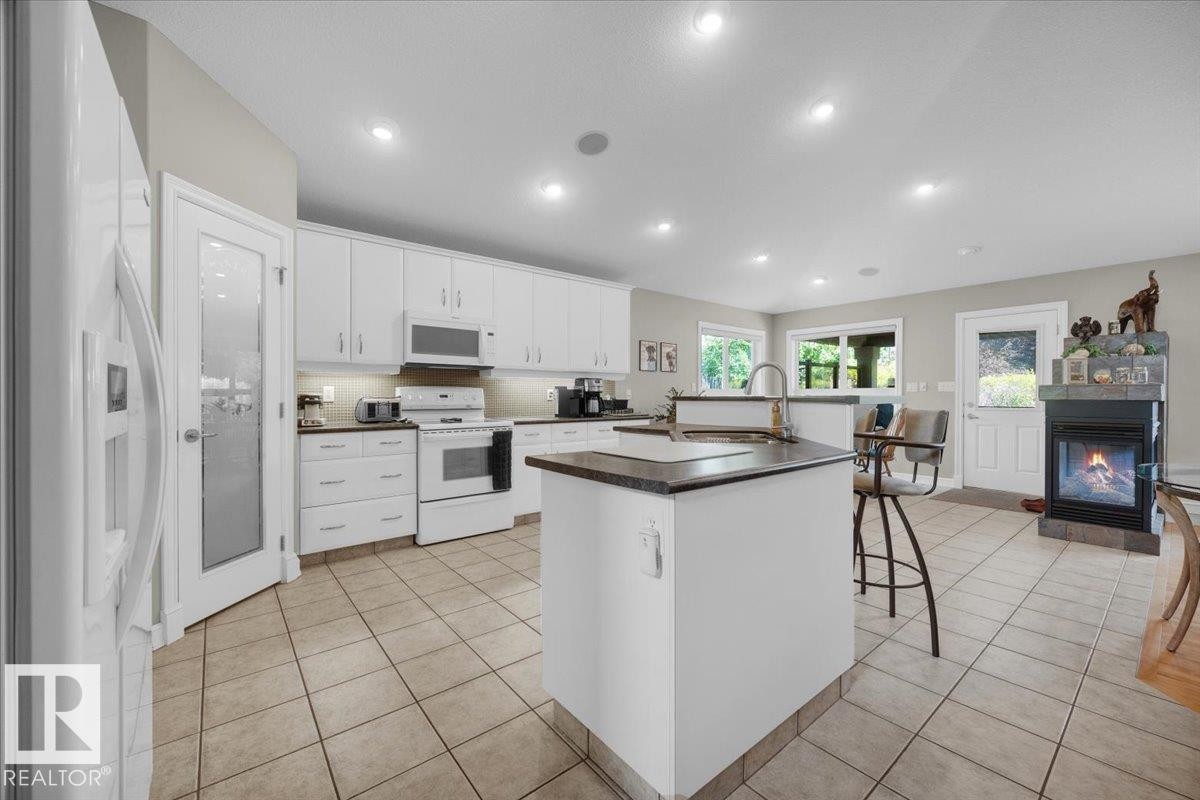 Expansive open-concept kitchen featuring a central island with sink, white cabinetry with under-cabinet lighting, and integrated white appliances - 928 Thompson Place Nw, Edmonton, AB - Indoor Photo Showing Kitchen