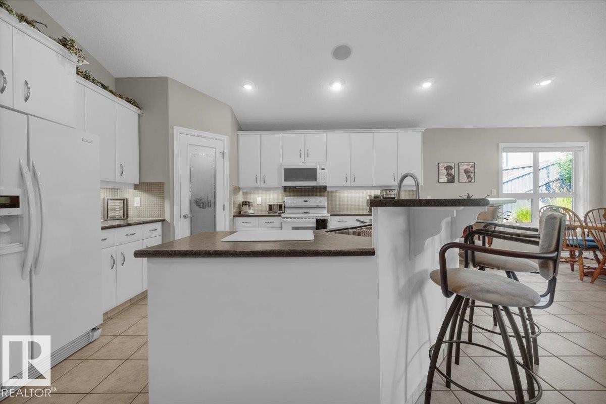 Kitchen featuring white cabinetry, an island with a breakfast bar, recessed lighting, tile flooring, and a sliding glass door - 928 Thompson Place Nw, Edmonton, AB - Indoor Photo Showing Kitchen