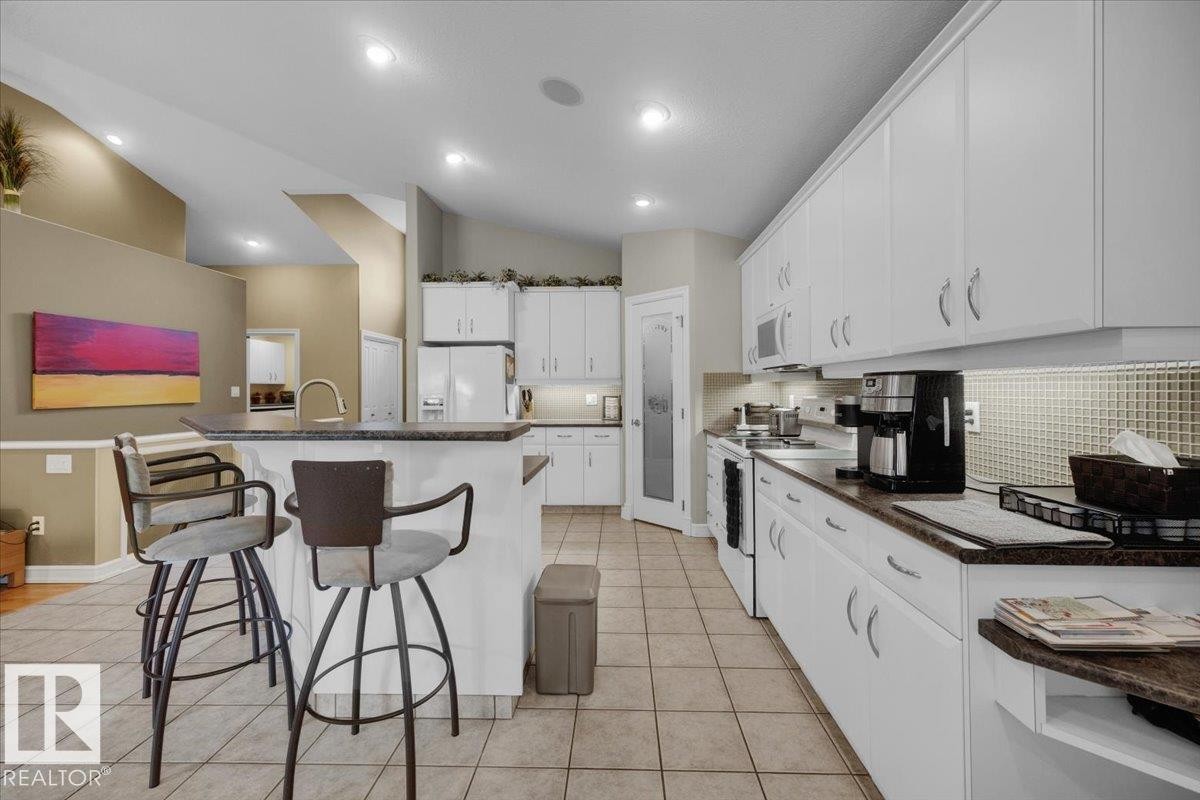 Kitchen featuring white cabinetry with silver-toned hardware, a tile backsplash, and a pantry with a frosted glass door - 928 Thompson Place Nw, Edmonton, AB - Indoor Photo Showing Kitchen