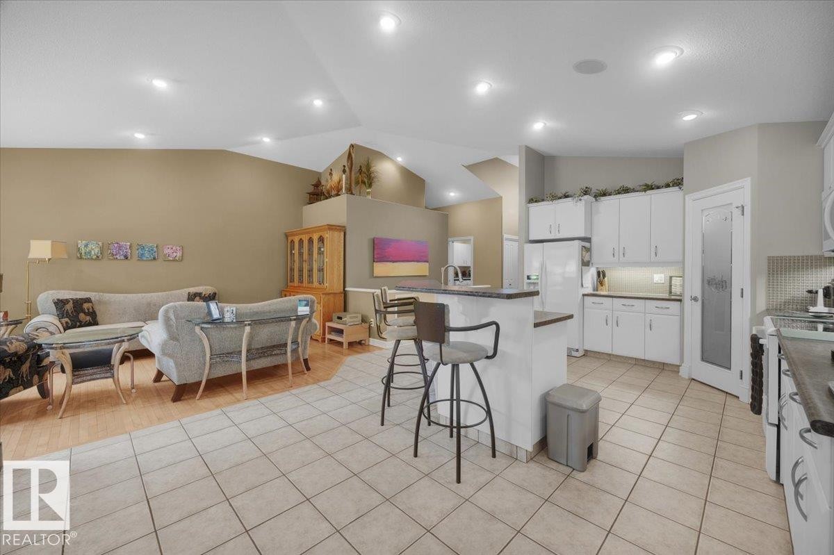 Open-concept living area and kitchen featuring vaulted ceilings, recessed lighting, tile flooring, white cabinetry, and a kitchen island with seating - 928 Thompson Place Nw, Edmonton, AB - Indoor Photo Showing Kitchen