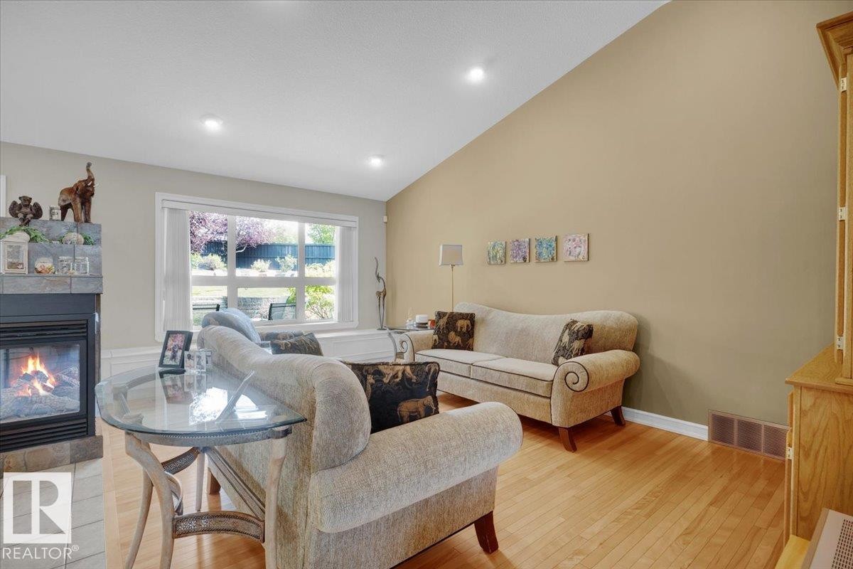 Living room featuring vaulted ceilings, light wood-finish flooring, recessed lighting, a fireplace with a tiled surround, and a large picture window - 928 Thompson Place Nw, Edmonton, AB - Indoor Photo Showing Living Room With Fireplace