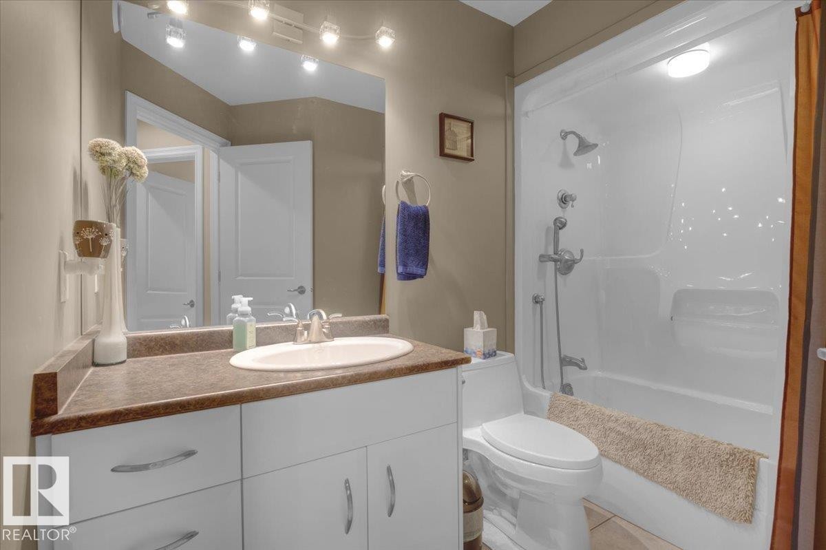 Full bathroom featuring a white vanity with an integrated sink, a dark countertop, white cabinetry with curved hardware, and a combination bathtub and shower with a single-handle faucet - 928 Thompson Place Nw, Edmonton, AB - Indoor Photo Showing Bathroom