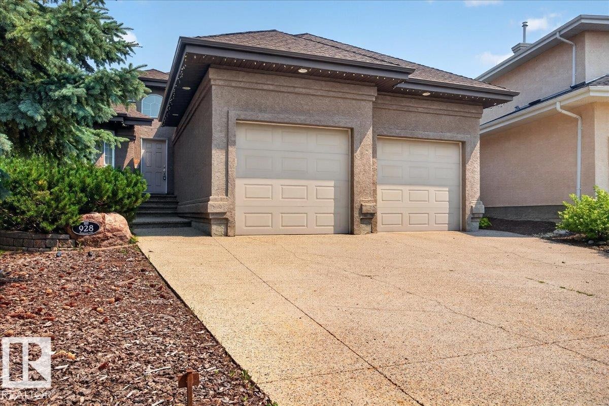 Exterior featuring a two-car garage, concrete driveway, front entrance steps, and diverse landscaping with mature trees and shrubs - 928 Thompson Place Nw, Edmonton, AB - Outdoor