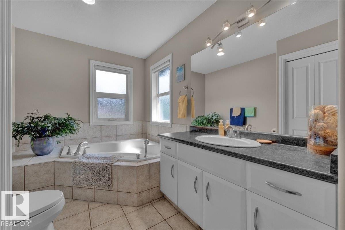 Bathroom featuring a built-in corner soaking tub with tile surround, a double-door closet, a vanity with a dark countertop and integrated sink, and track lighting above the mirror - 928 Thompson Place Nw, Edmonton, AB - Indoor Photo Showing Bathroom