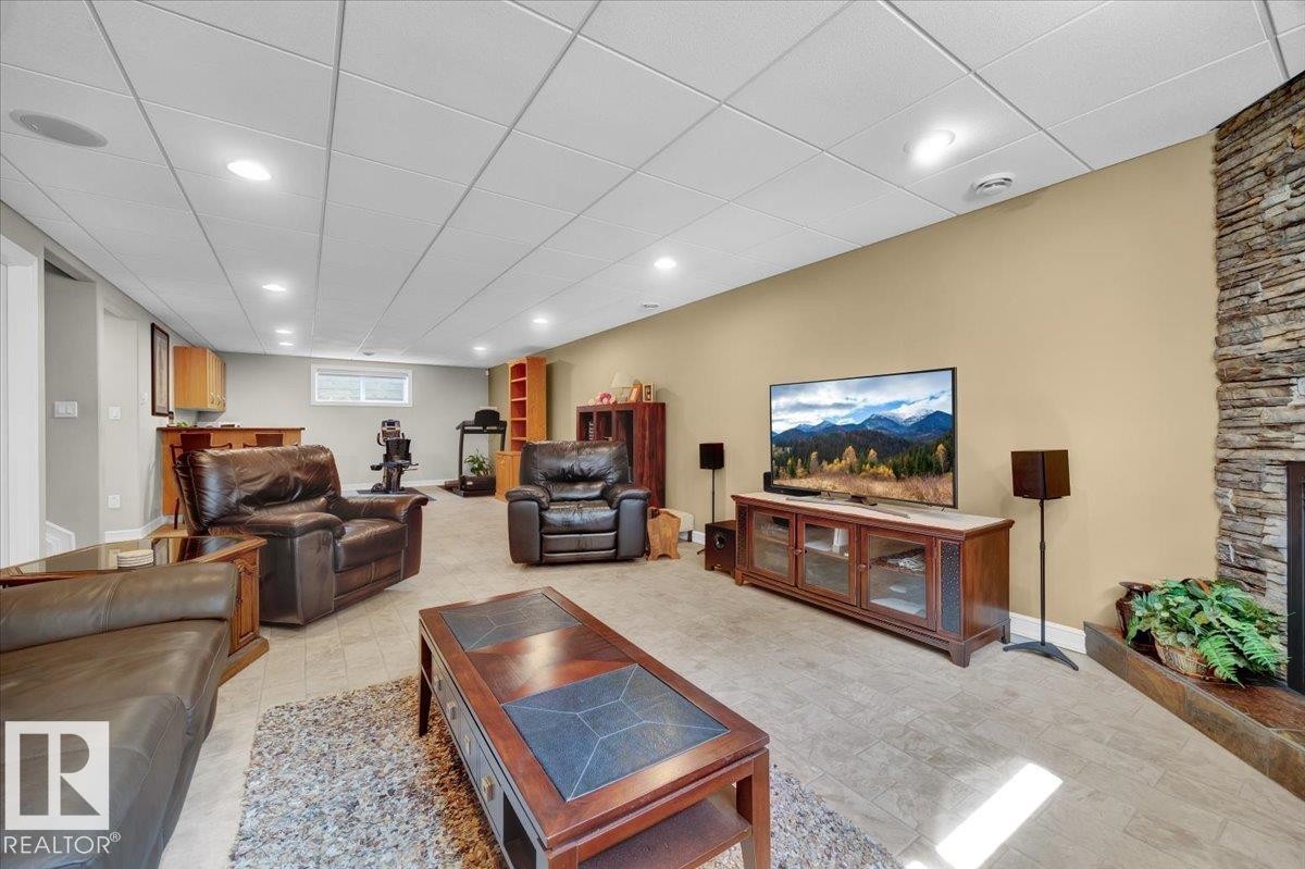 Spacious entertainment room featuring a stacked stone fireplace, tile flooring, recessed lighting, and a drop ceiling - 928 Thompson Place Nw, Edmonton, AB - Indoor