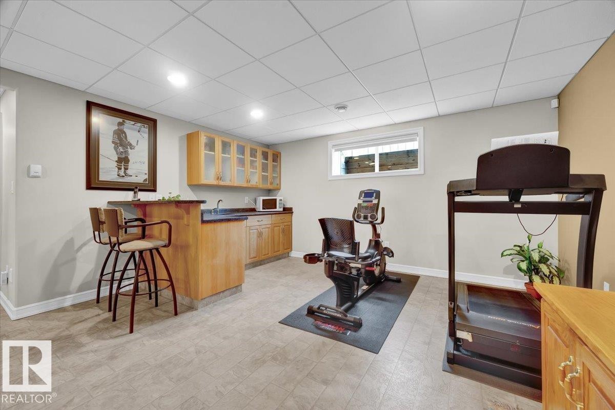 Lower level recreational space featuring a built-in wet bar with wood cabinetry, a dark countertop, and an undermount sink - 928 Thompson Place Nw, Edmonton, AB - Indoor