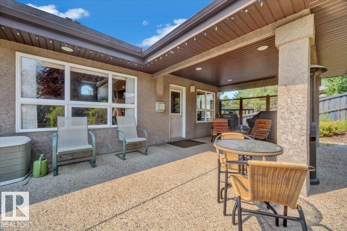 Expansive covered patio featuring an exposed aggregate surface, stucco exterior walls, a built-in outdoor heater, white-framed windows, and a glass privacy fence - 928 Thompson Place Nw, Edmonton, AB - Outdoor With Deck Patio Veranda With Exterior