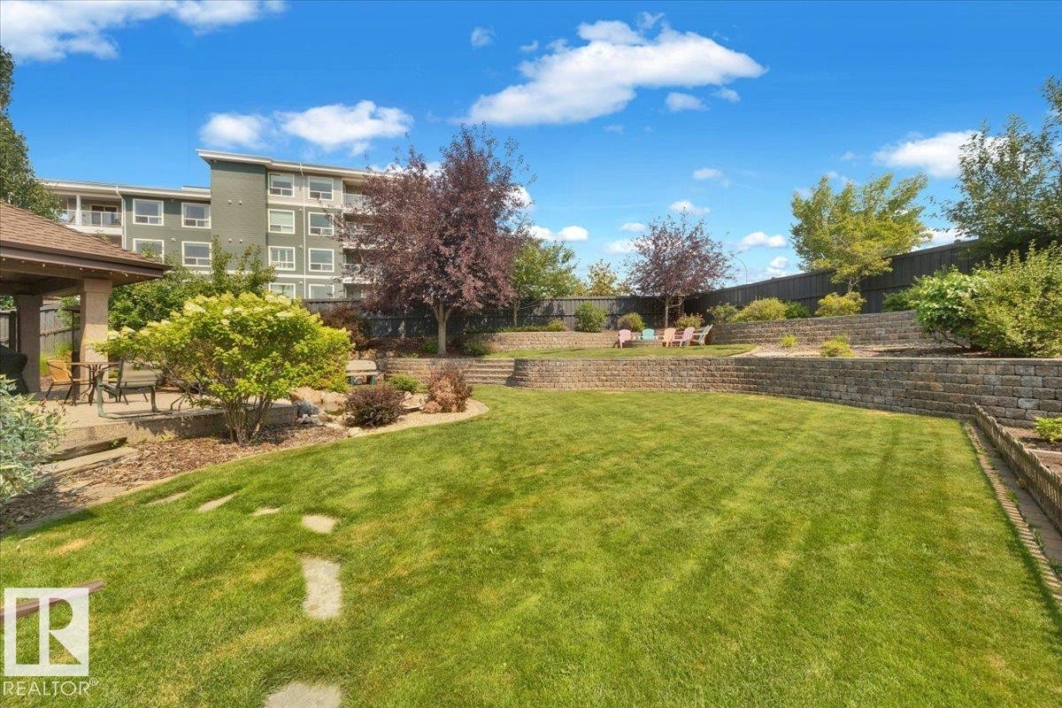 Expansive backyard featuring a manicured lawn, tiered retaining walls, mature trees, a covered patio, and stepping stones - 928 Thompson Place Nw, Edmonton, AB - Outdoor
