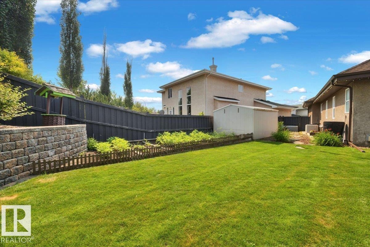 Expansive backyard featuring a lush lawn, a stone retaining wall, and a black privacy fence - 928 Thompson Place Nw, Edmonton, AB - Outdoor