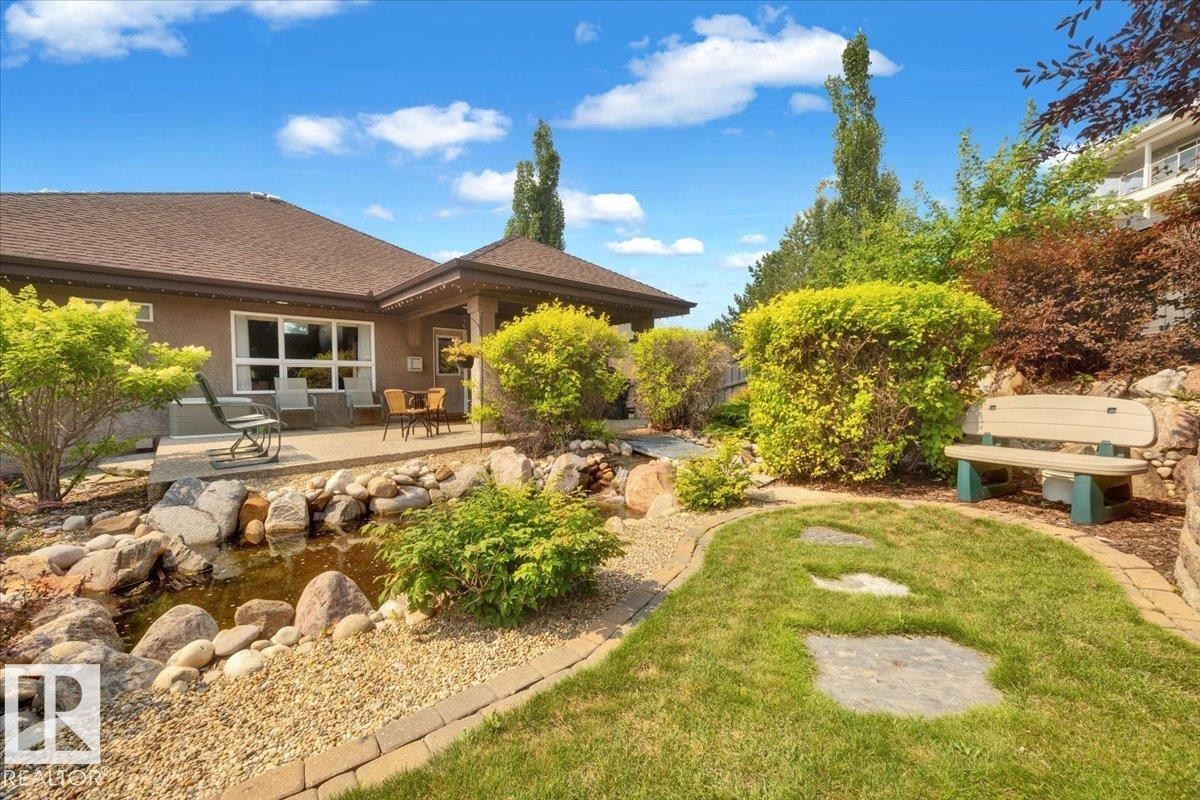 Landscaped backyard featuring a stone-lined pond, a paved patio area, and mature shrubbery - 928 Thompson Place Nw, Edmonton, AB - Outdoor