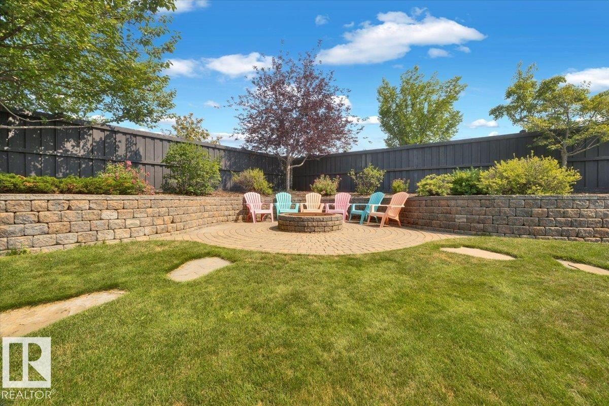 Expansive backyard featuring a circular paver patio with a built-in fire pit, surrounded by tiered stone retaining walls and mature landscaping - 928 Thompson Place Nw, Edmonton, AB - Outdoor With Backyard