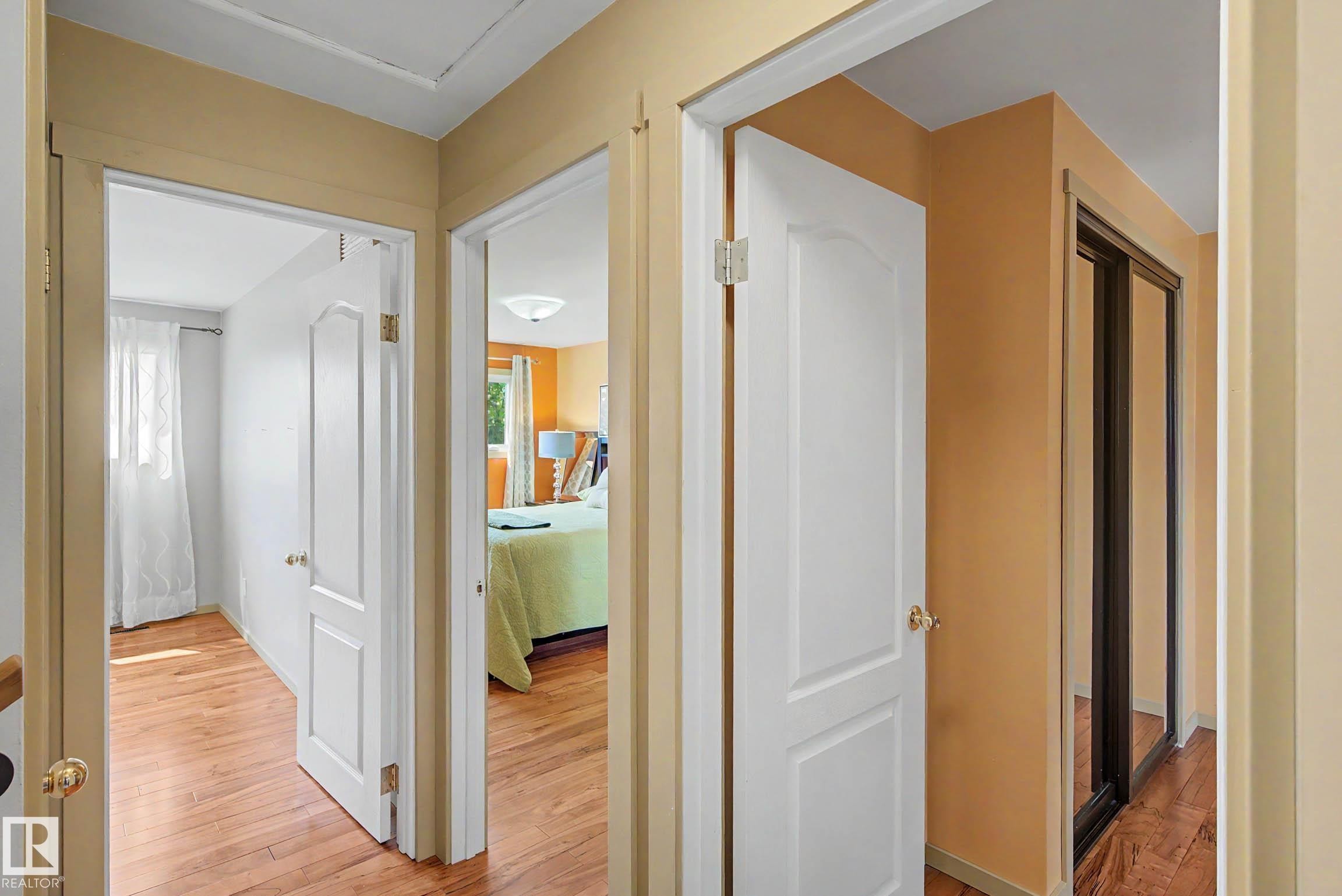 Interior hallway featuring wood-finish flooring, white paneled doors with brass hardware, and light-toned wall paint - 9516 129A Avenue Nw, Edmonton, AB