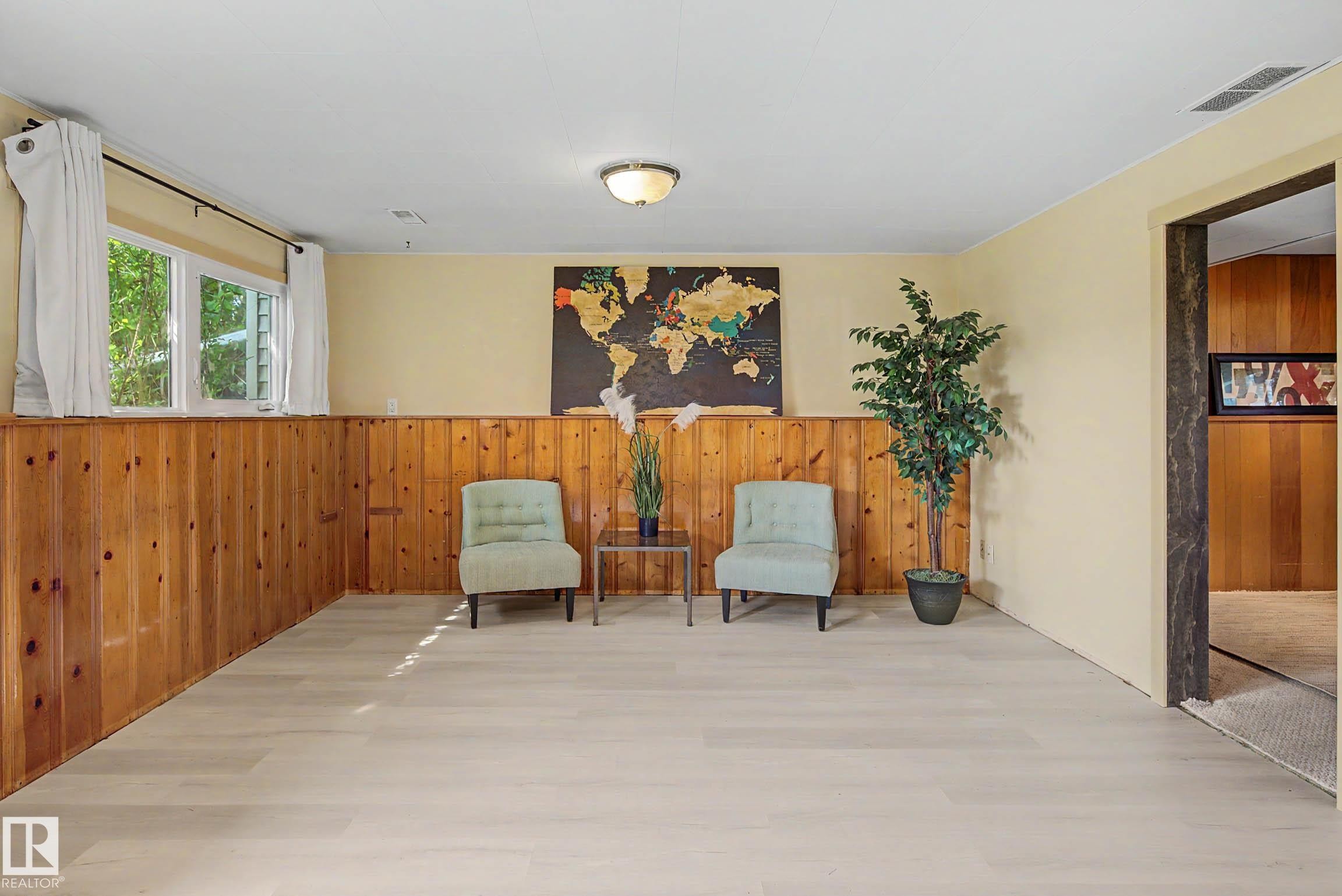 Spacious room featuring light wood-finish flooring, natural wood paneling, and a contemporary ceiling light fixture - 9516 129A Avenue Nw, Edmonton, AB