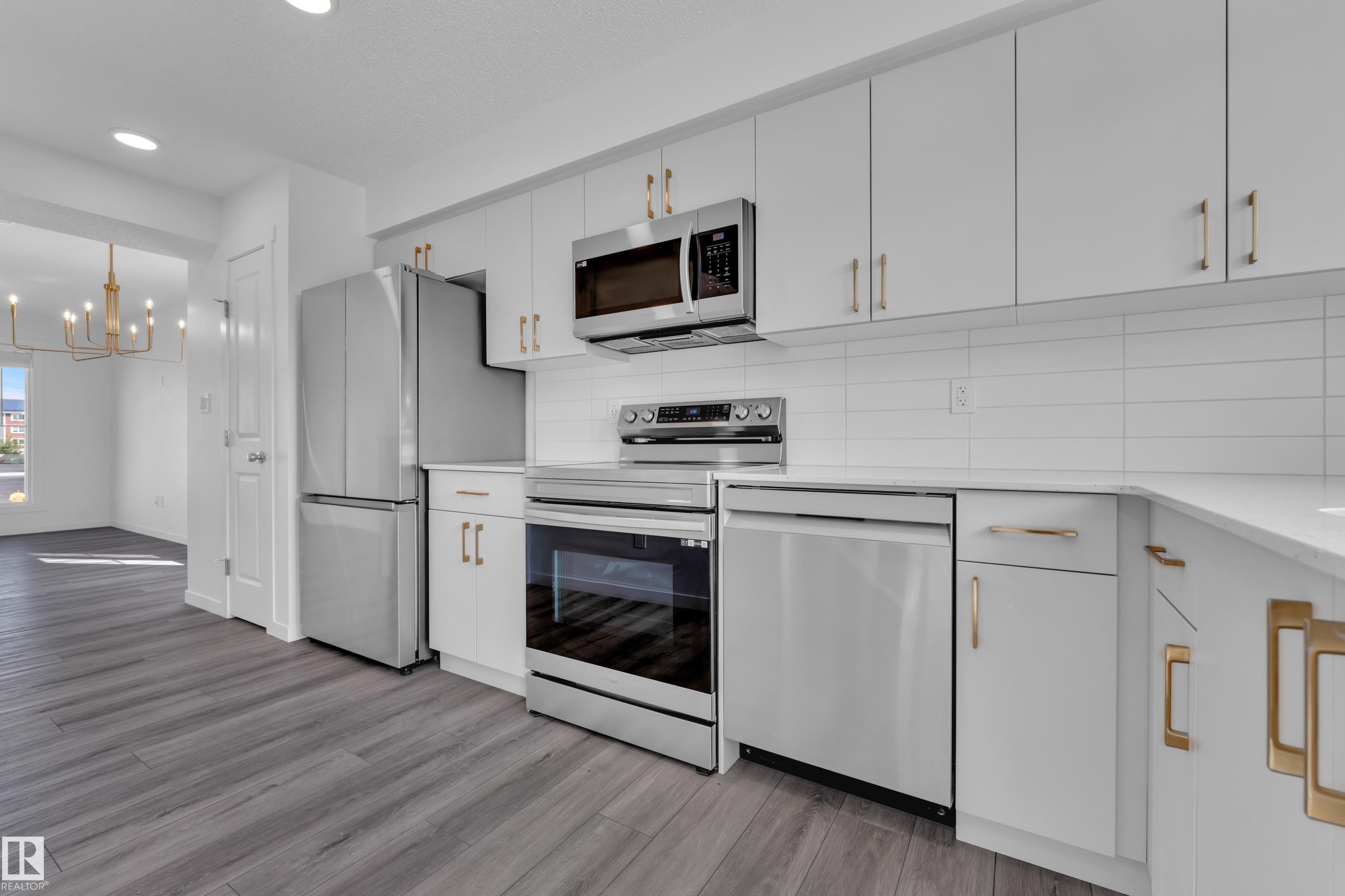 Modern kitchen featuring stainless steel appliances, white cabinetry with gold-tone hardware, white subway tile backsplash, and wood-finish flooring - #64 17832 78 St Nw Nw, Edmonton, AB - Indoor Photo Showing Kitchen