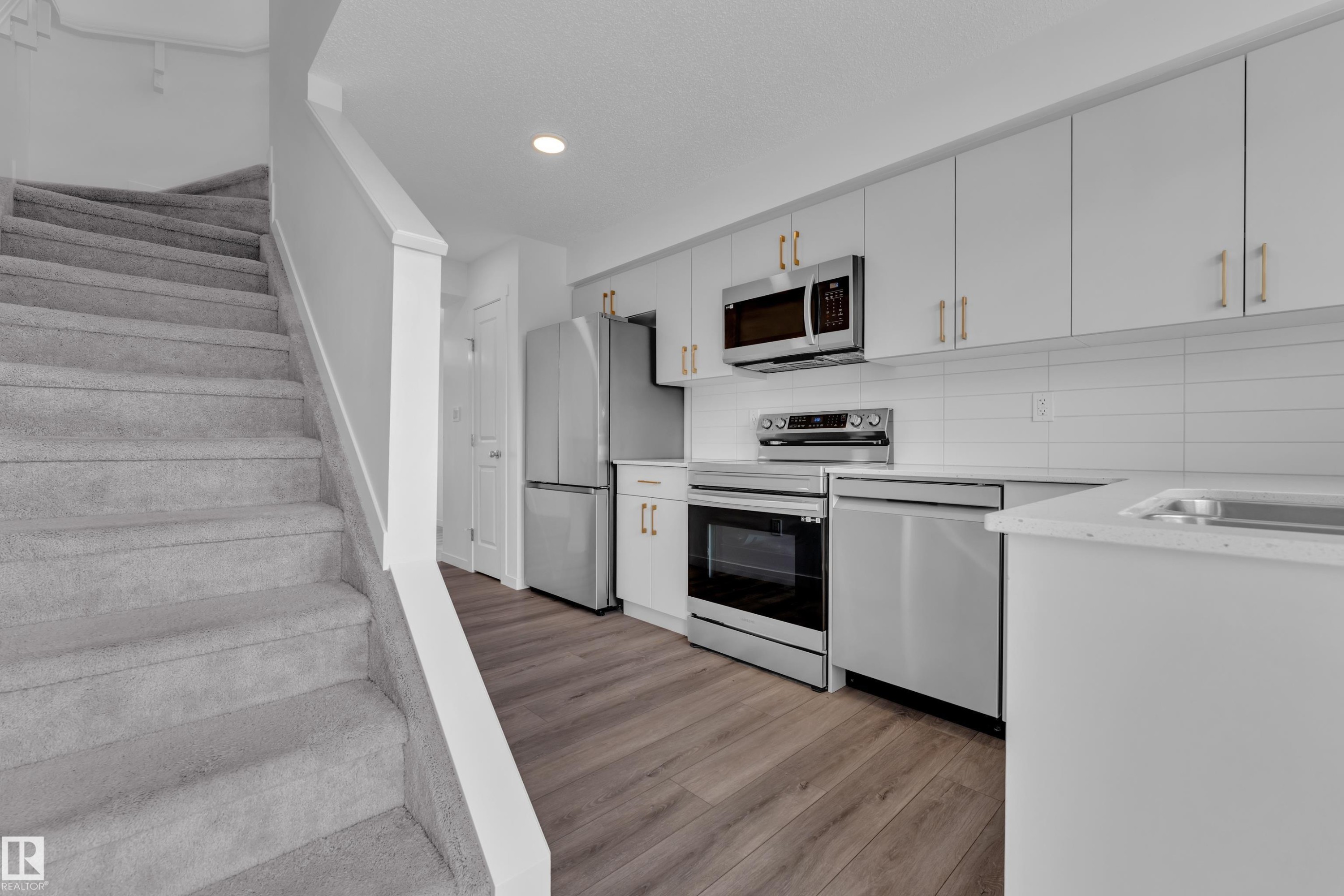 Modern kitchen featuring white cabinetry with gold-finish hardware, stainless steel appliances, and white subway tile backsplash - #64 17832 78 St Nw Nw, Edmonton, AB - Indoor Photo Showing Kitchen