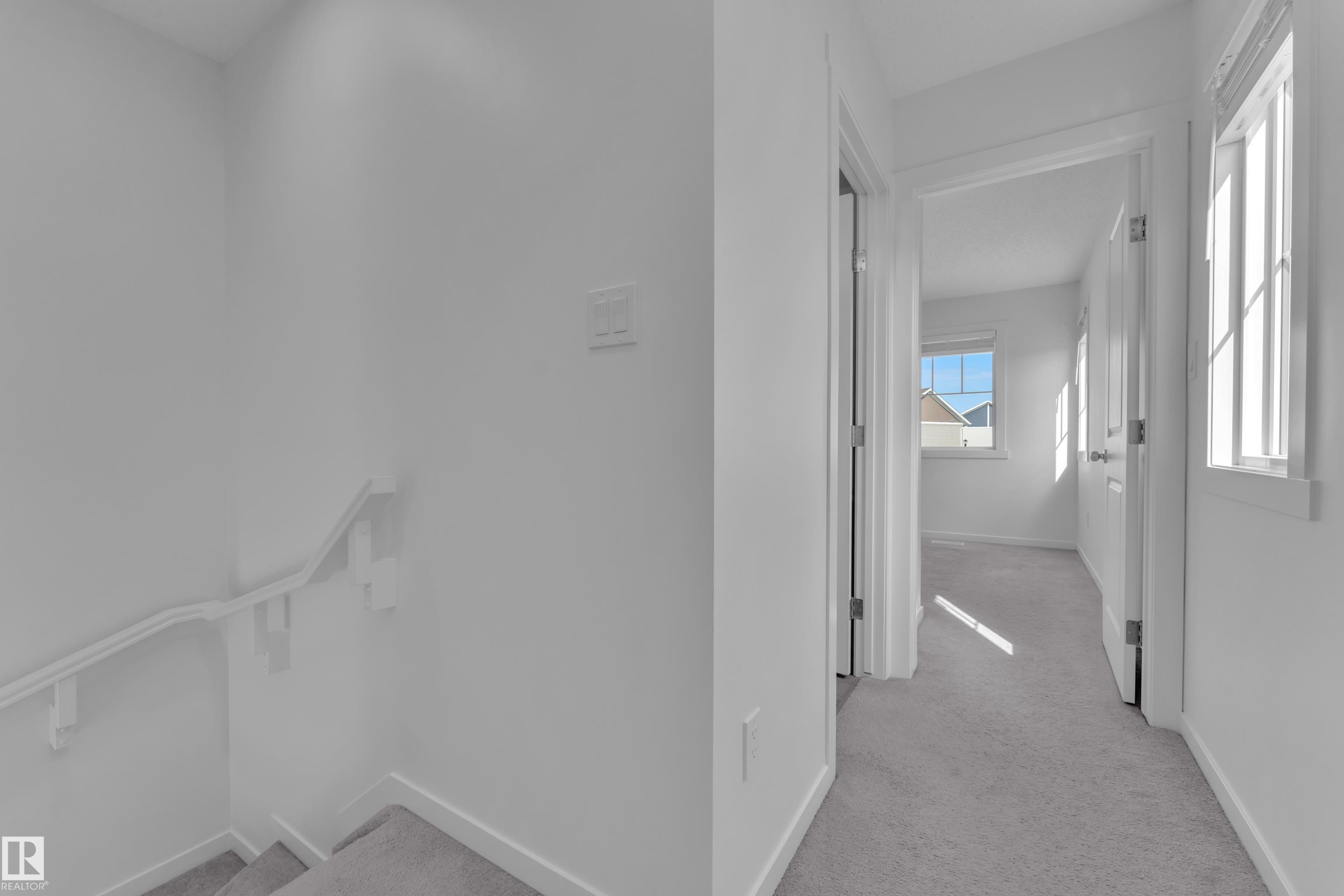 Hallway with light gray carpeting, white walls, and bright natural light from multiple windows - #64 17832 78 St Nw Nw, Edmonton, AB - Indoor Photo Showing Other Room
