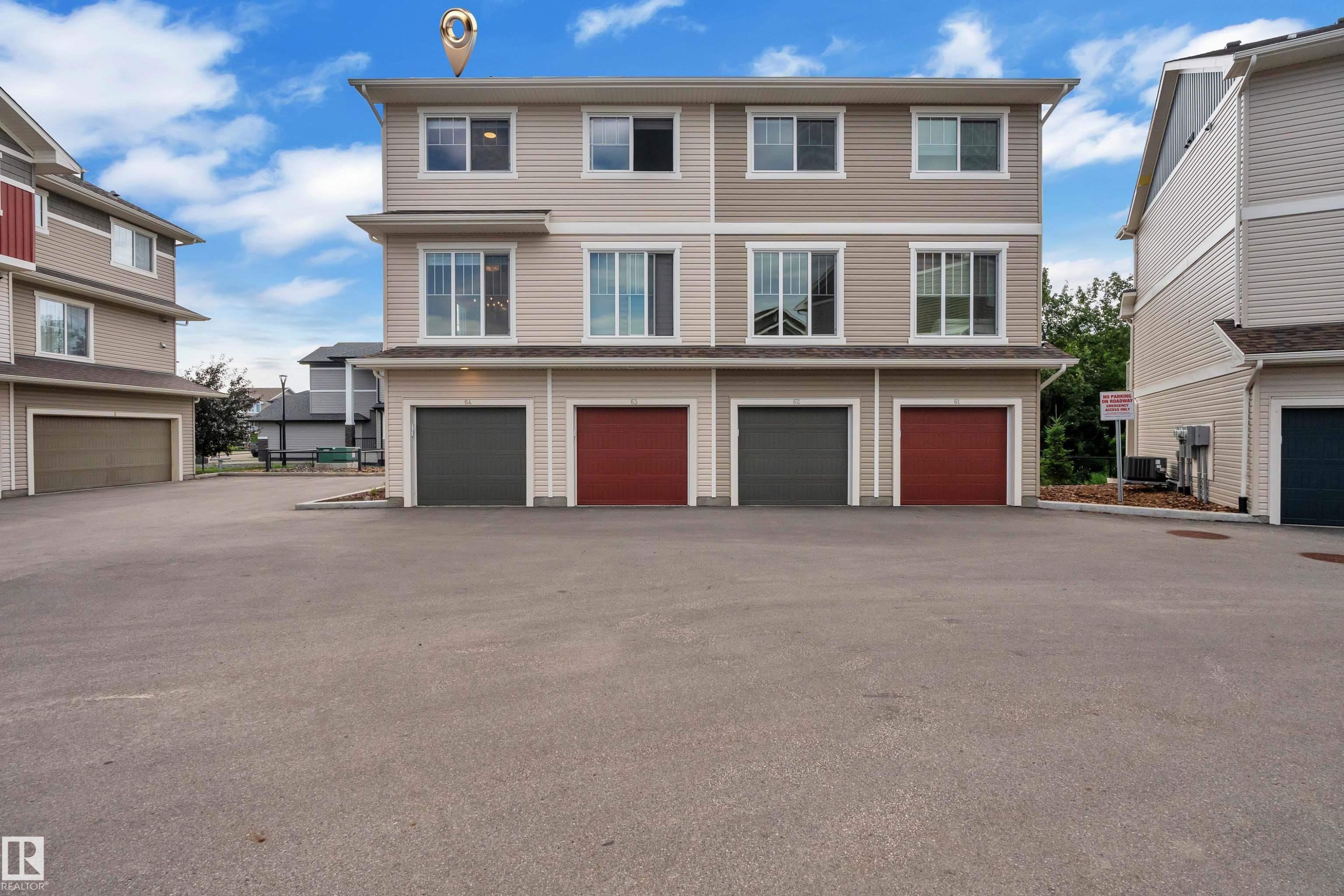Multi-level exterior featuring light-toned siding, multiple windows, and two distinct garage doors - #64 17832 78 St Nw Nw, Edmonton, AB - Outdoor With Facade