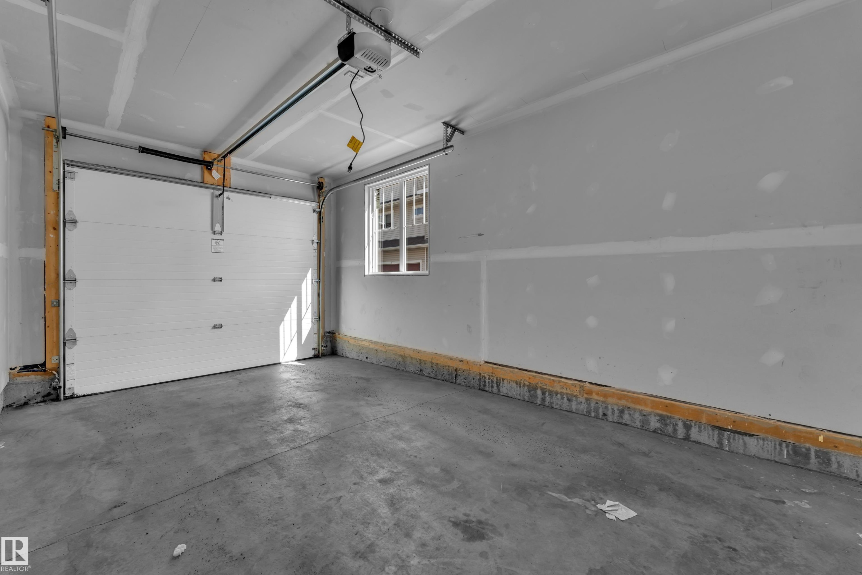 Spacious garage featuring a concrete floor, white panel garage door, automatic opener, and a single window - #64 17832 78 St Nw Nw, Edmonton, AB - Indoor Photo Showing Garage
