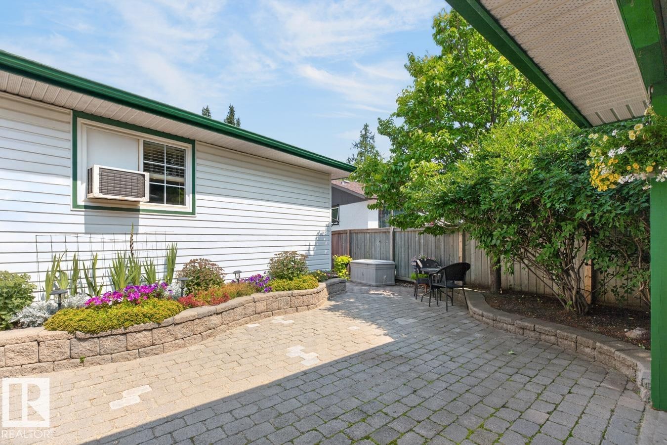 Stone paver patio featuring a hot tub, wood privacy fence, and mature trees - 27 Milford Crescent, Sherwood Park, AB - Outdoor With Exterior