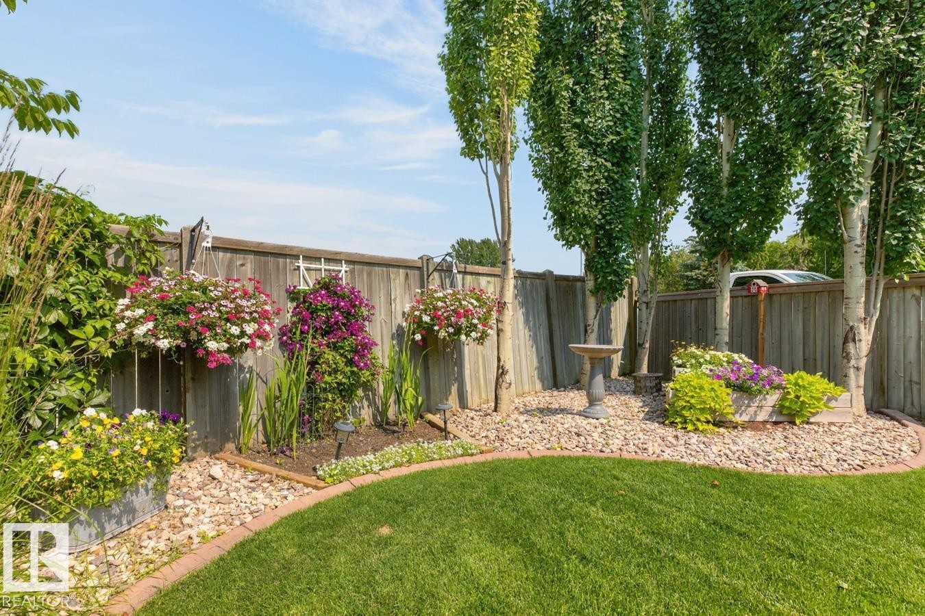 Expansive lawn area with a curved brick border, mature trees, and a decorative bird bath - 27 Milford Crescent, Sherwood Park, AB - Outdoor