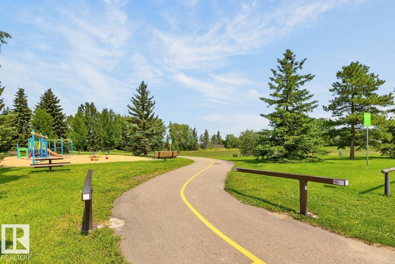 Paved pathway winding through a green space featuring mature evergreen trees and a sand-based playground with colorful equipment - 27 Milford Crescent, Sherwood Park, AB - Outdoor With View