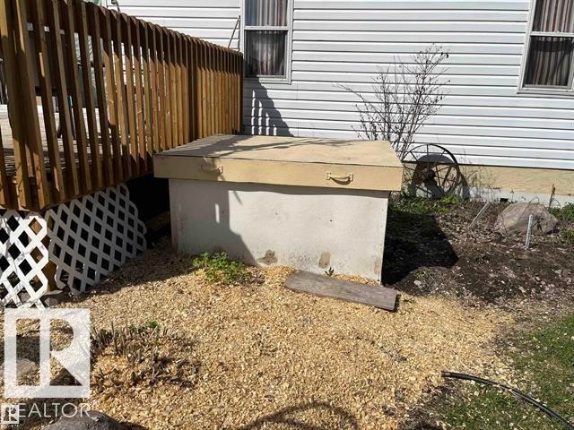 Concrete utility access with a top-mounted handle, situated alongside a wood deck with lattice skirting and white vinyl siding - 210 55504 Nikoodi Road, Rural Lac Ste. Anne County, AB - Outdoor
