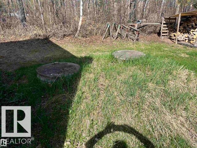 Grassy outdoor area featuring two circular concrete covers, a wood storage structure, and surrounding natural foliage - 210 55504 Nikoodi Road, Rural Lac Ste. Anne County, AB - Outdoor