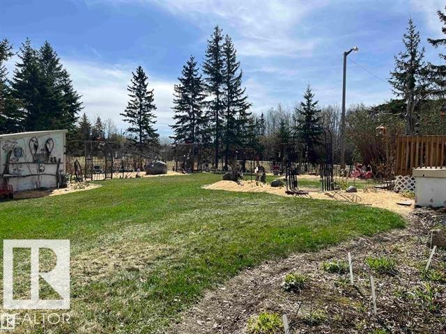 Spacious outdoor area featuring a grassy lawn, mature evergreen trees, a garden shed with artistic detailing, a gravel pathway, and a privacy fence - 210 55504 Nikoodi Road, Rural Lac Ste. Anne County, AB - Outdoor