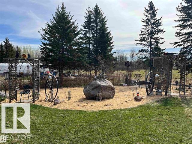 Manicured lawn area featuring a decorative wood chip bed with a large central rock formation, flanked by tall evergreen trees - 210 55504 Nikoodi Road, Rural Lac Ste. Anne County, AB - Outdoor