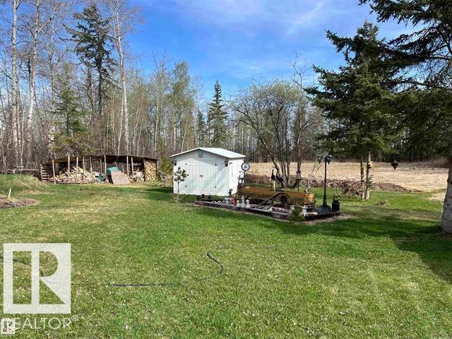 Spacious backyard featuring a manicured lawn, white storage shed, and a rustic wood storage structure - 210 55504 Nikoodi Road, Rural Lac Ste. Anne County, AB - Outdoor