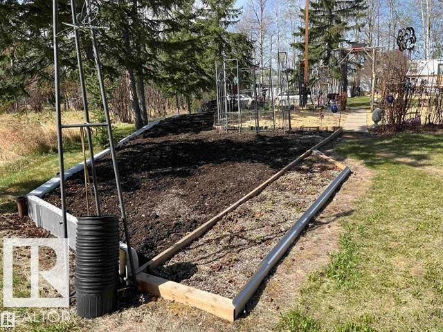 Raised garden bed with dark soil, bordered by wood and concrete, featuring a metal trellis - 210 55504 Nikoodi Road, Rural Lac Ste. Anne County, AB - Outdoor