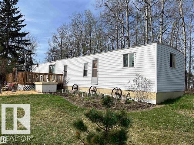 White siding exterior with a wood deck, mature trees, and a garden area - 210 55504 Nikoodi Road, Rural Lac Ste. Anne County, AB - Outdoor