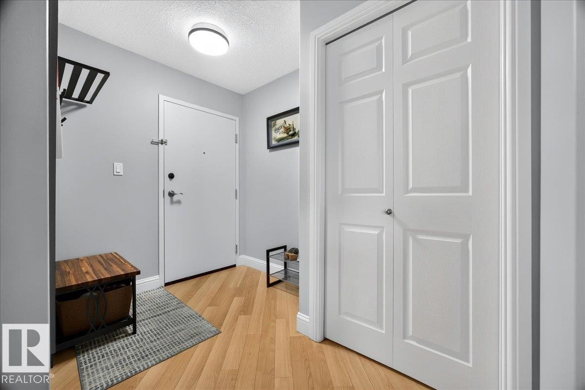 Entryway featuring wood-finish flooring, light gray wall paint, a flush-mount ceiling light, and a white paneled bi-fold closet door - #306 13111 140 Av Nw, Edmonton, AB - Indoor Photo Showing Other Room