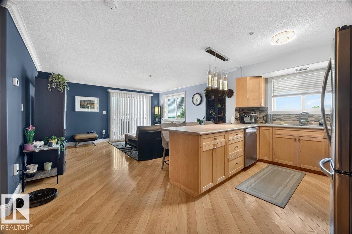 Open-concept living space featuring wood-finish flooring, a kitchen island with natural wood cabinetry, stainless steel appliances, and a glass sliding door - #306 13111 140 Av Nw, Edmonton, AB - Indoor Photo Showing Kitchen