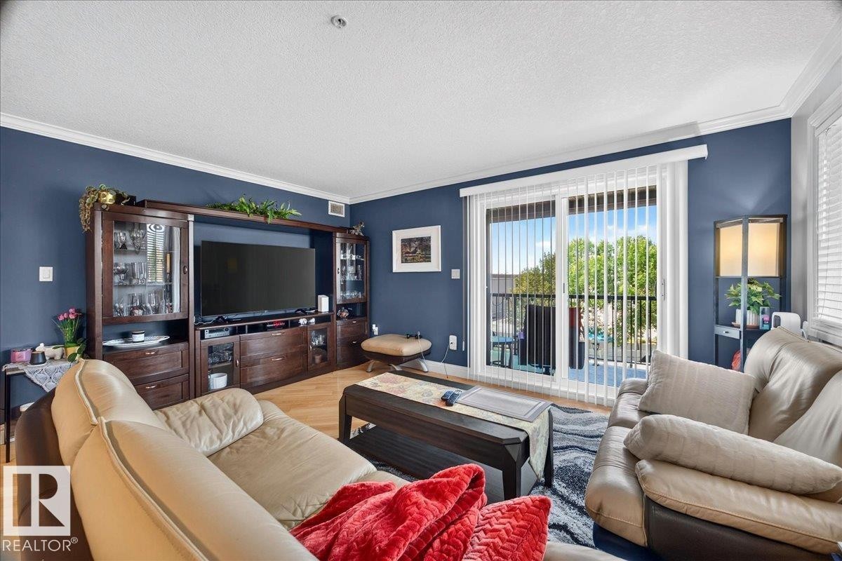 Living area featuring a sliding glass door to a private balcony, wood-finish flooring, a built-in media console, crown molding, and painted accent walls - #306 13111 140 Av Nw, Edmonton, AB - Indoor Photo Showing Living Room