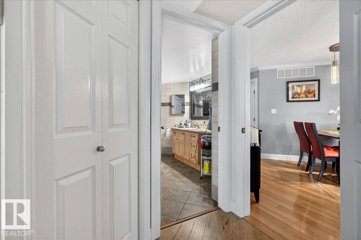 White bi-fold doors frame a hallway with wood-finish flooring - #306 13111 140 Av Nw, Edmonton, AB - Indoor Photo Showing Other Room