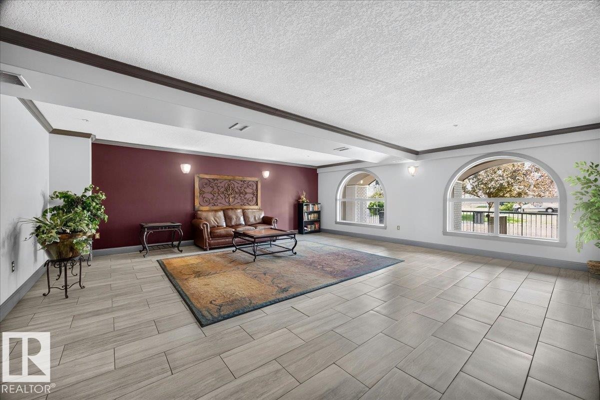 Spacious room featuring light-toned tile flooring, two arched windows, a burgundy accent wall with sconce lighting, and dark crown molding - #306 13111 140 Av Nw, Edmonton, AB - Indoor Photo Showing Other Room