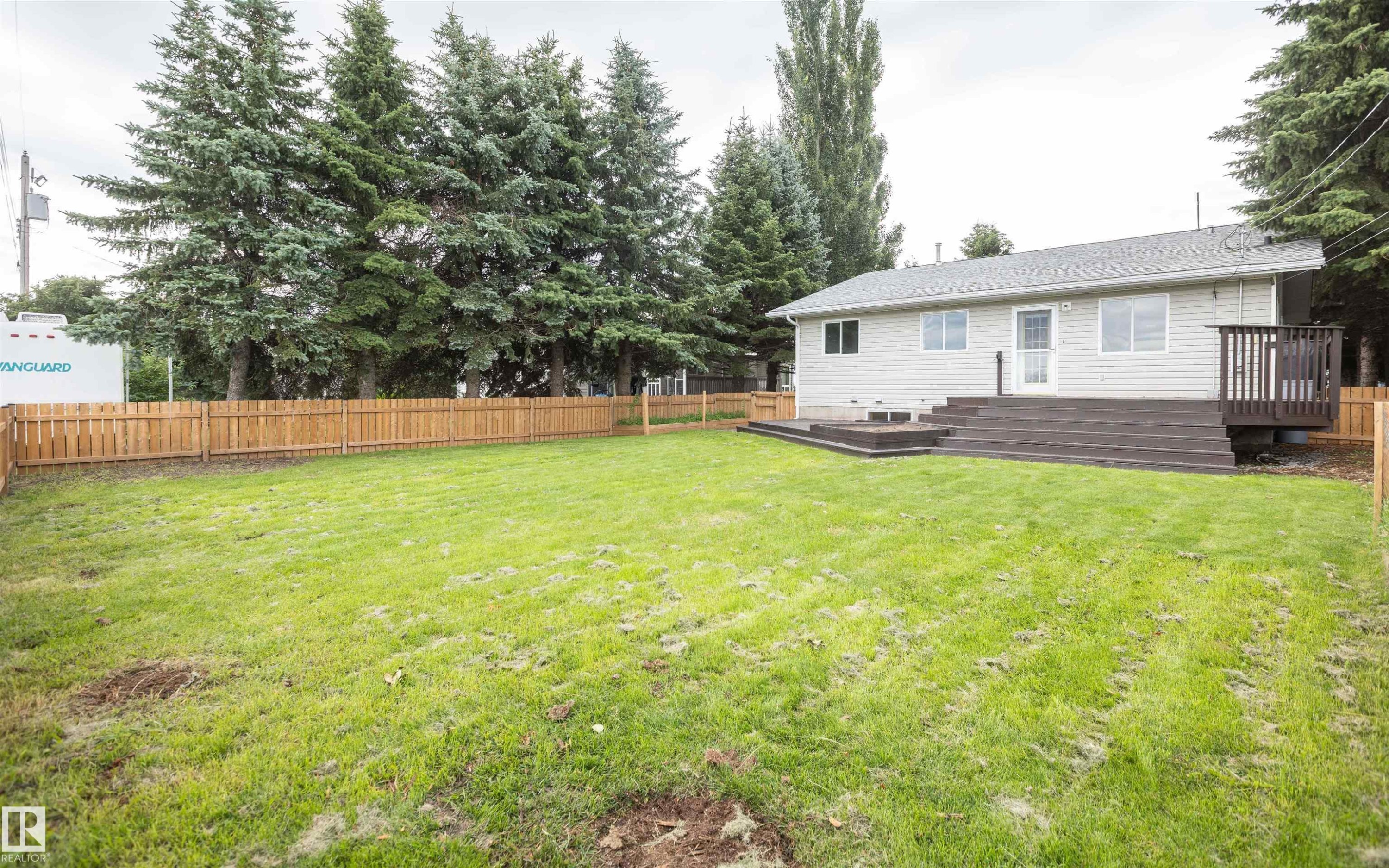Rear exterior featuring light-colored siding, a multi-level dark-toned deck, and a privacy fence - 5116 51 Avenue, Pickardville, AB - Outdoor