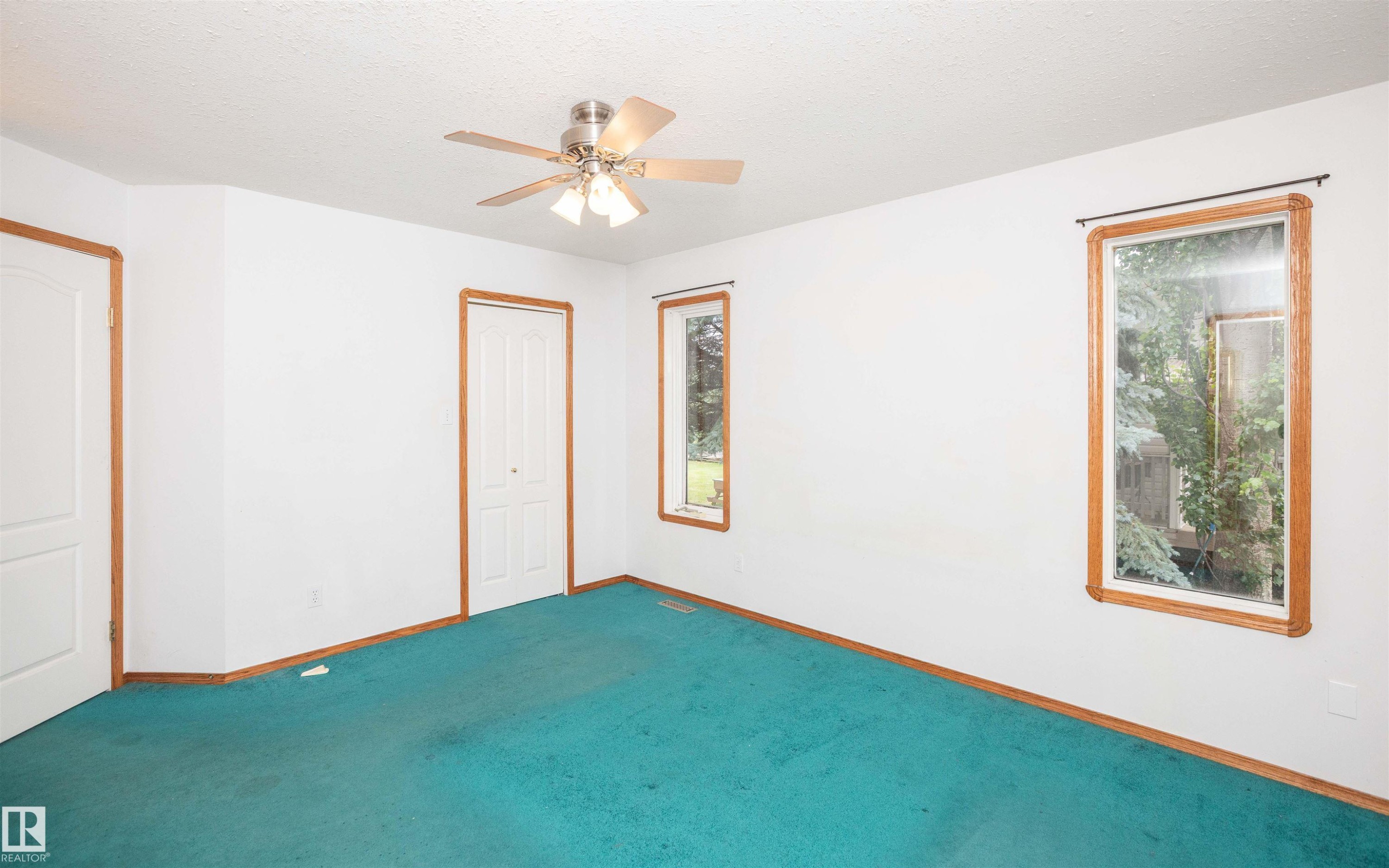 Spacious room featuring a ceiling fan with integrated lighting, wood-trimmed windows, and a vibrant teal carpet - 5116 51 Avenue, Pickardville, AB - Indoor Photo Showing Other Room