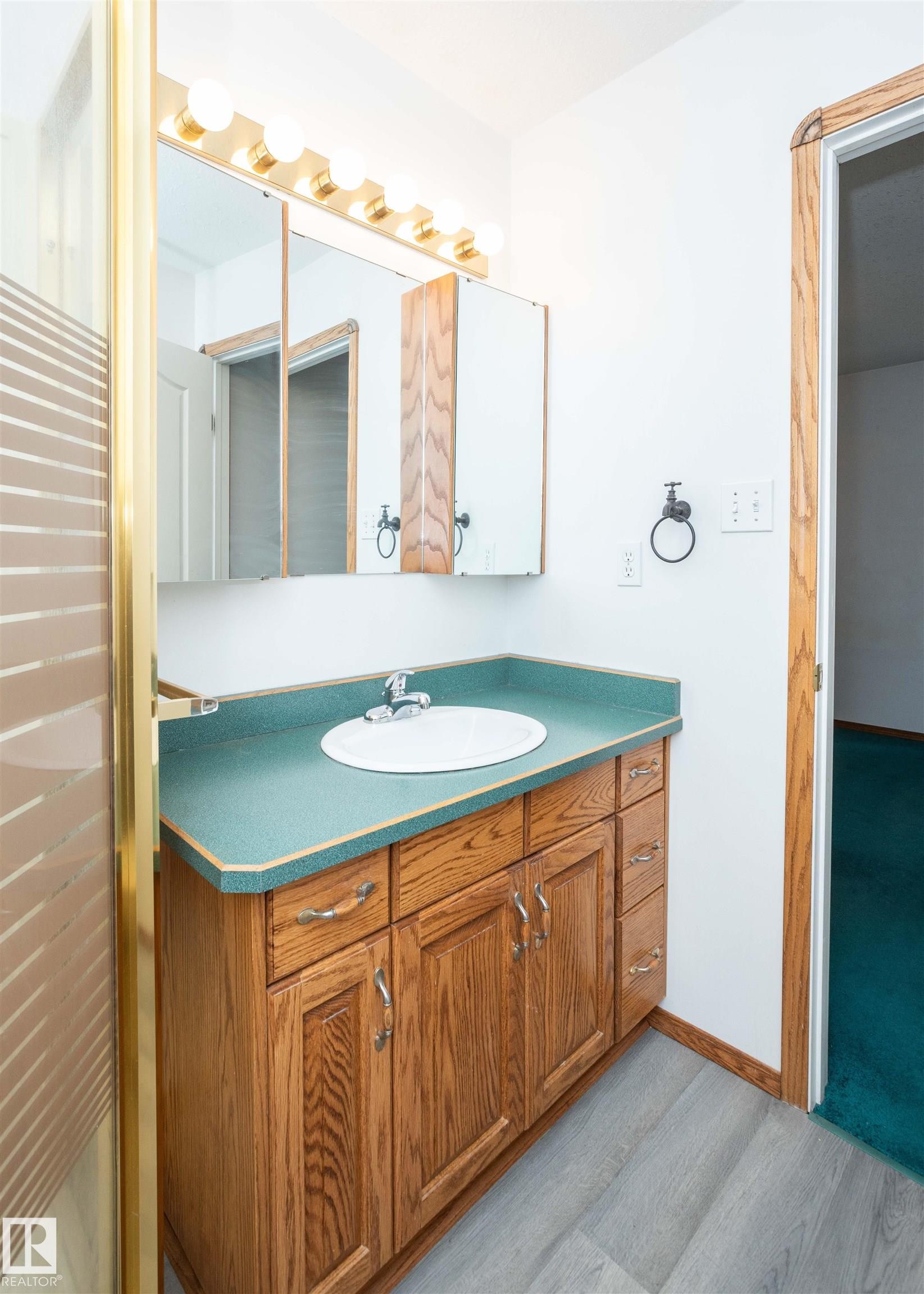 Bathroom vanity featuring a wood-finish cabinet with chrome hardware, an integrated sink, and a contrasting countertop - 5116 51 Avenue, Pickardville, AB - Indoor Photo Showing Bathroom