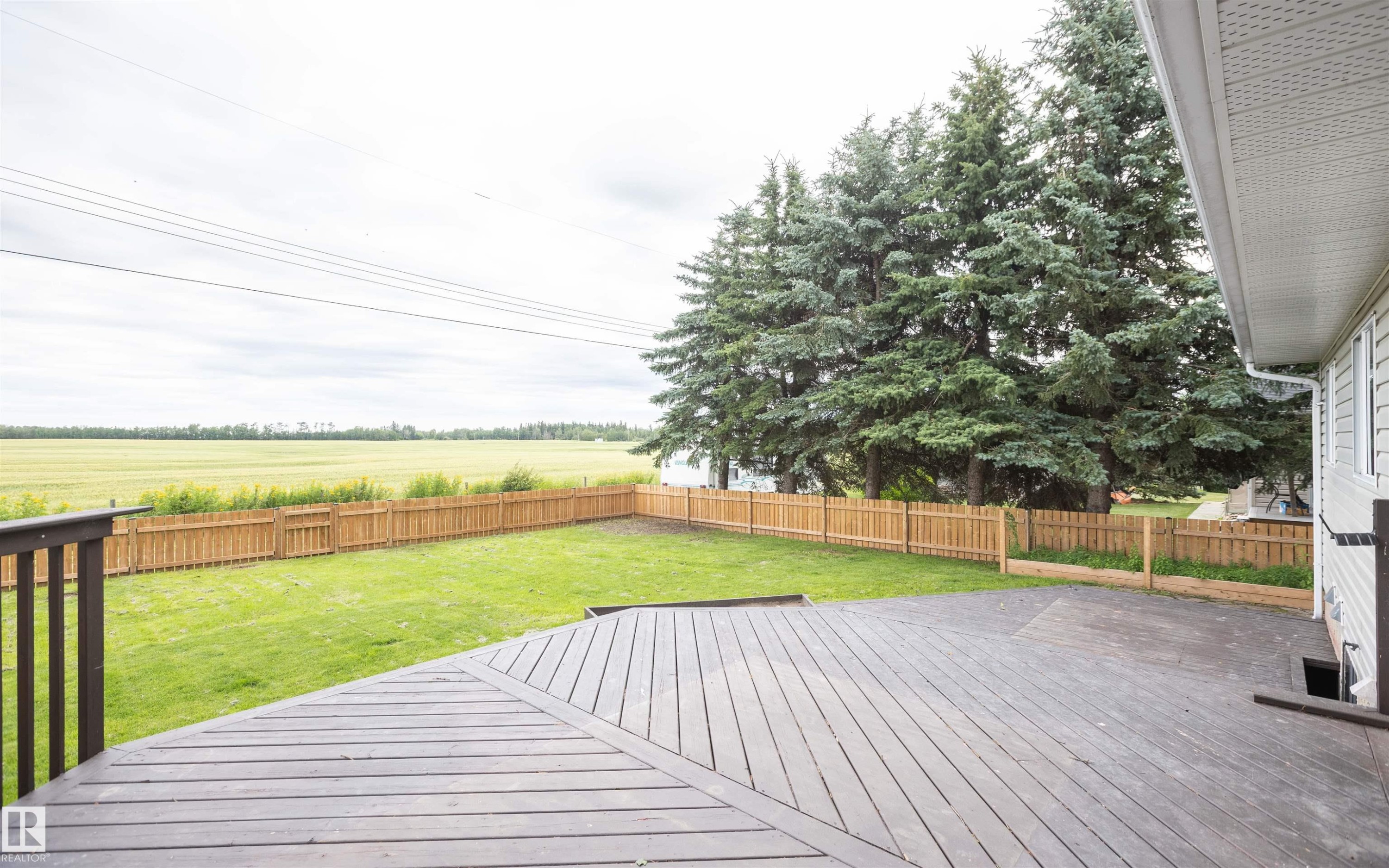 Expansive backyard featuring a multi-level composite deck, wooden privacy fence, mature evergreen trees, and a manicured lawn backing onto open fields - 5116 51 Avenue, Pickardville, AB - Outdoor With Deck Patio Veranda