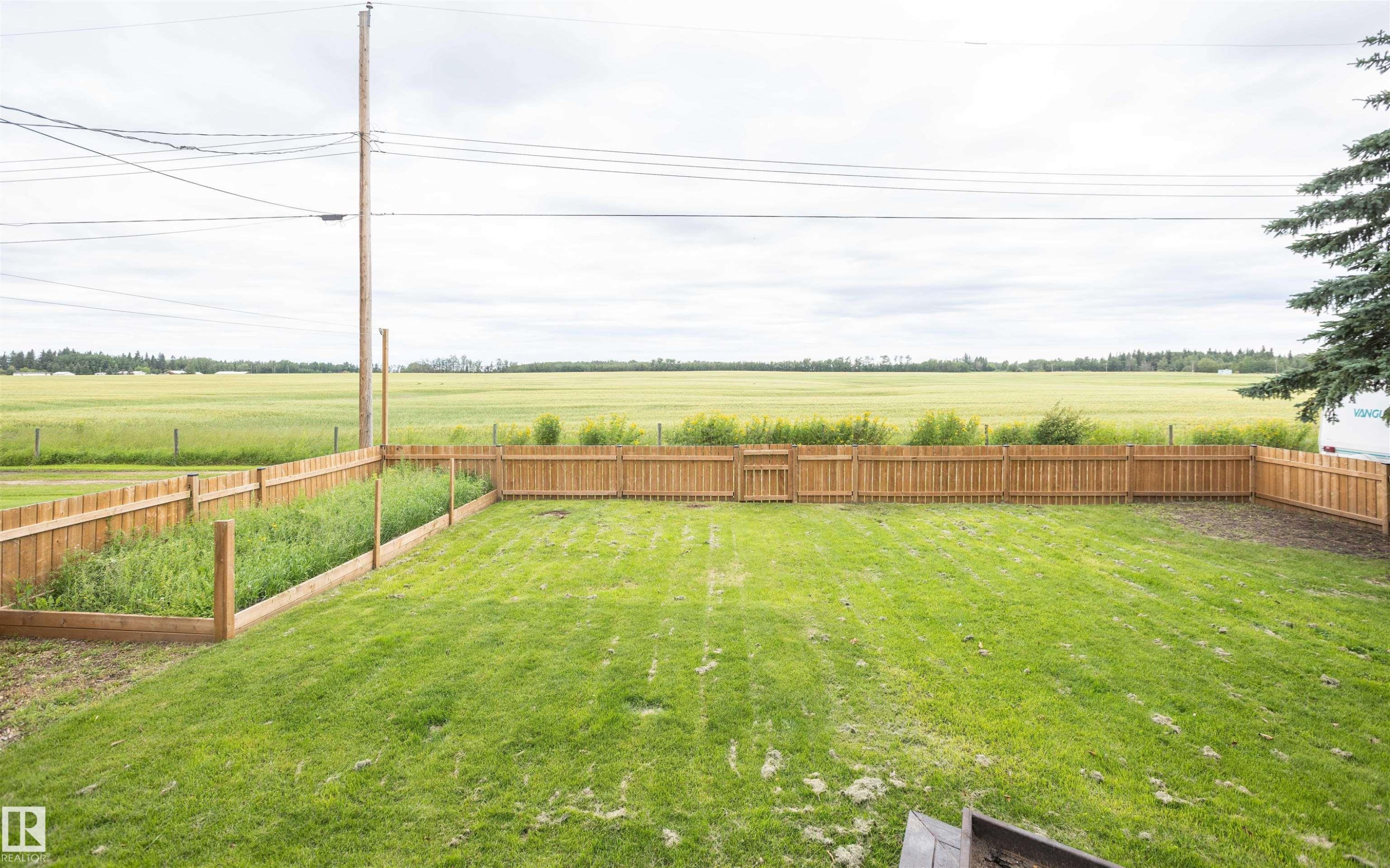 Expansive fenced backyard featuring a wood privacy fence, a dedicated garden area, and a large grassy lawn - 5116 51 Avenue, Pickardville, AB - Outdoor With View