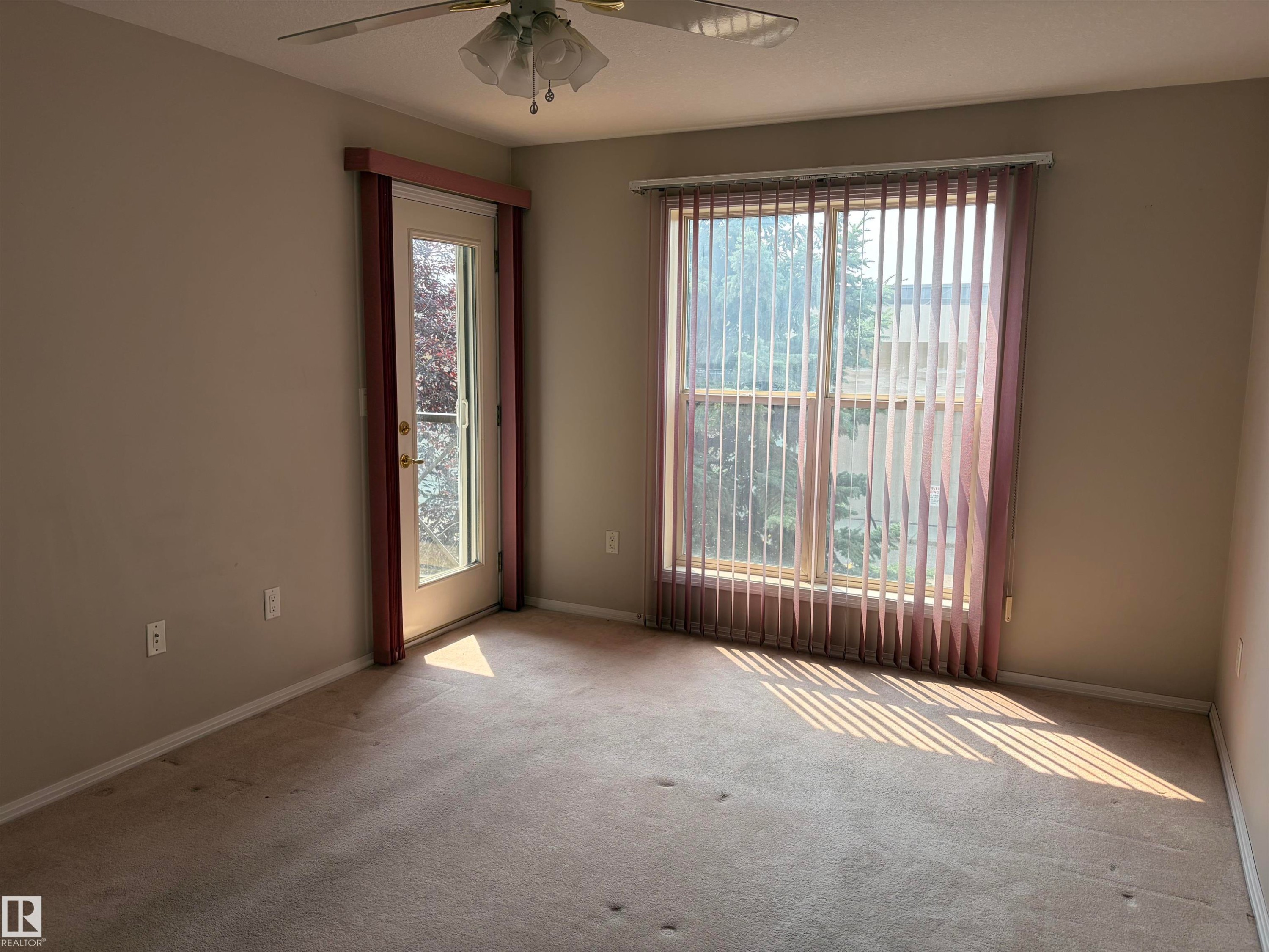 Carpeted room featuring a ceiling fan with integrated lighting, a glass-paneled door with dark trim, and a window with vertical blinds - #209 8912 156 St Nw, Edmonton, AB - Indoor Photo Showing Other Room