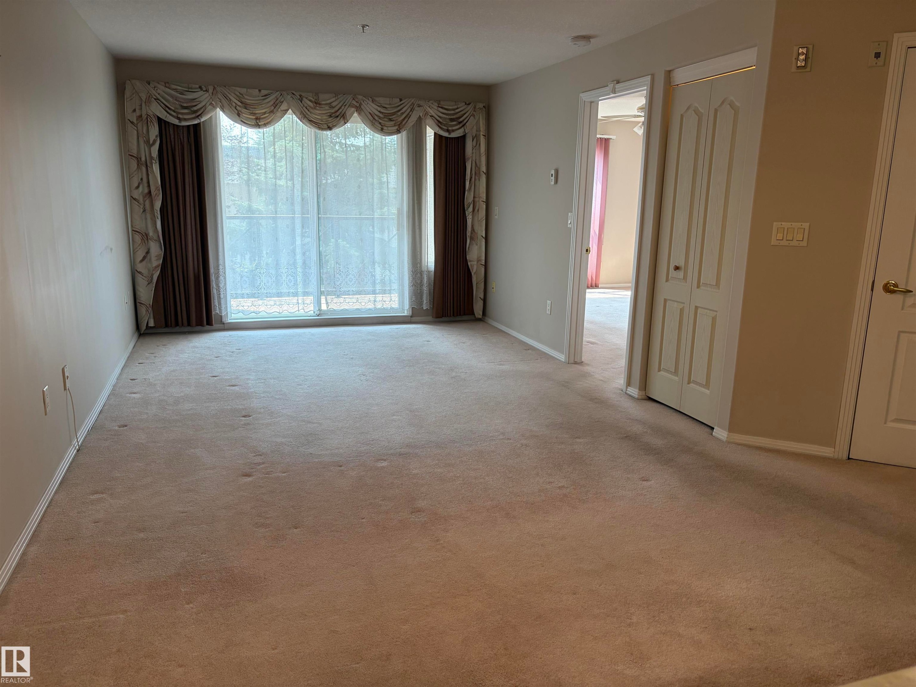 Spacious room featuring neutral carpeting, light-toned walls, and a wide sliding glass door - #209 8912 156 St Nw, Edmonton, AB - Indoor Photo Showing Other Room