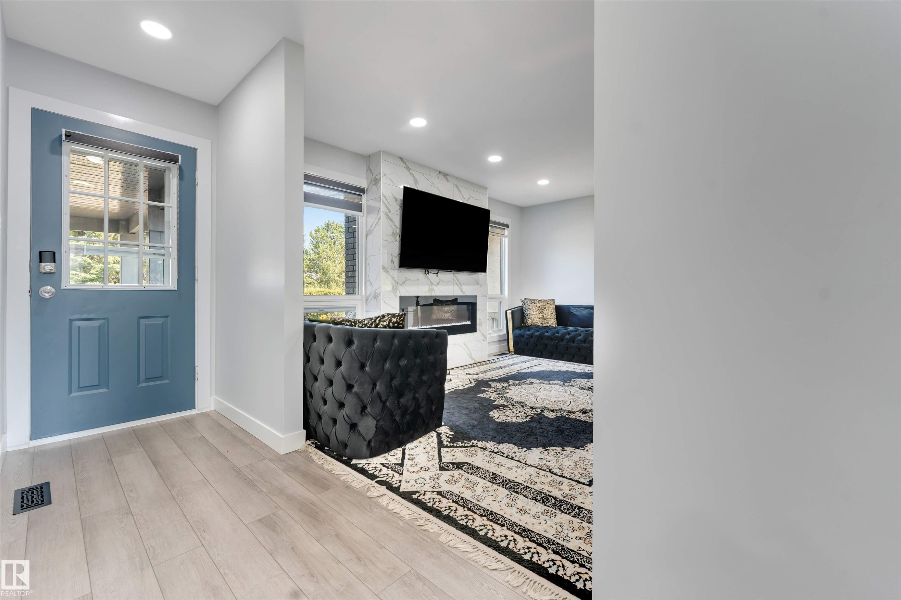 Entryway with light wood-finish flooring and a blue paneled door with glass inserts - 7419 33 Avenue Nw, Edmonton, AB - Indoor Photo Showing Other Room With Fireplace