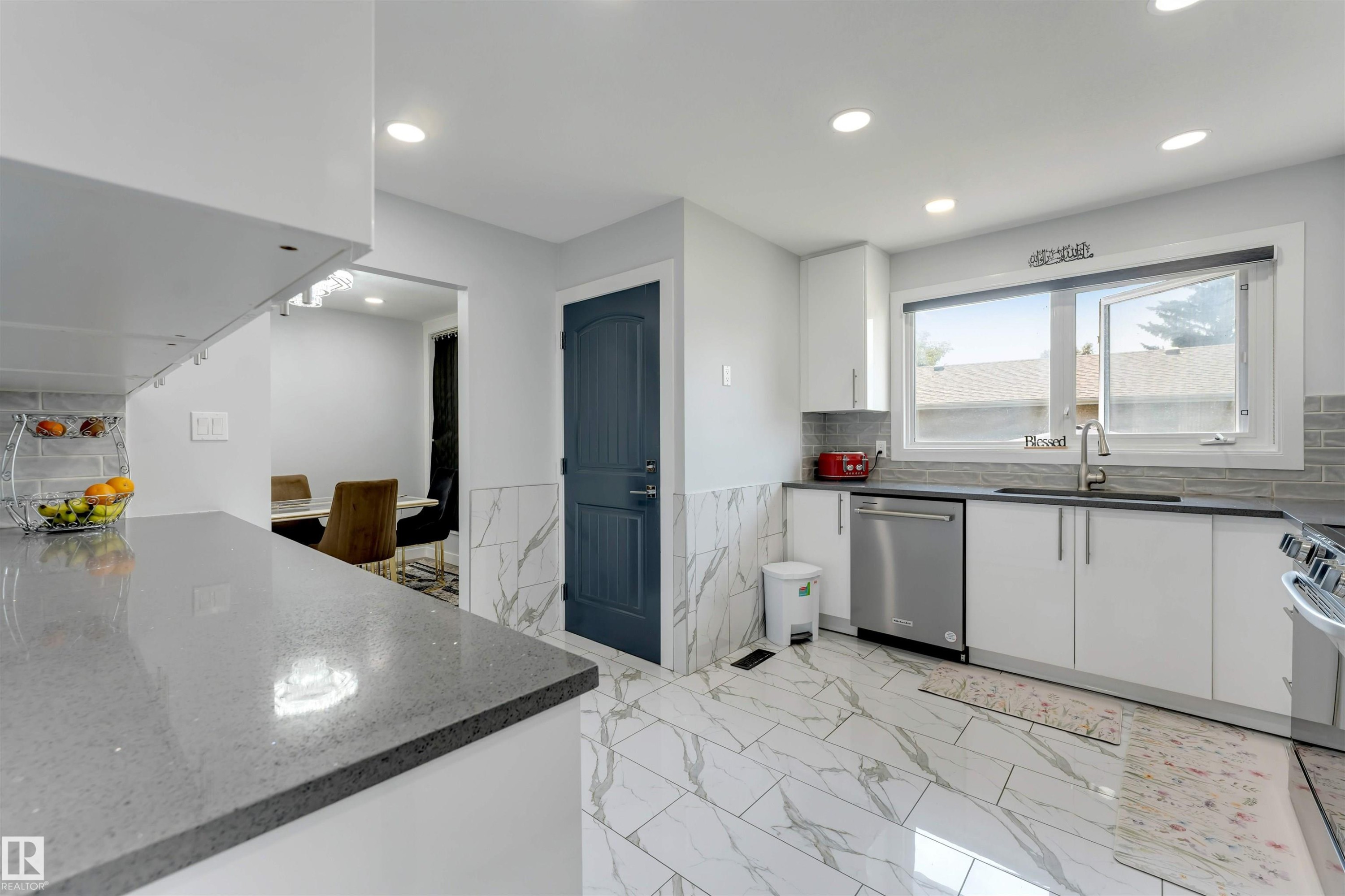 Contemporary kitchen featuring white cabinetry, grey stone countertops, stainless steel appliances, and large format marble-look floor tiles - 7419 33 Avenue Nw, Edmonton, AB - Indoor Photo Showing Kitchen With Upgraded Kitchen