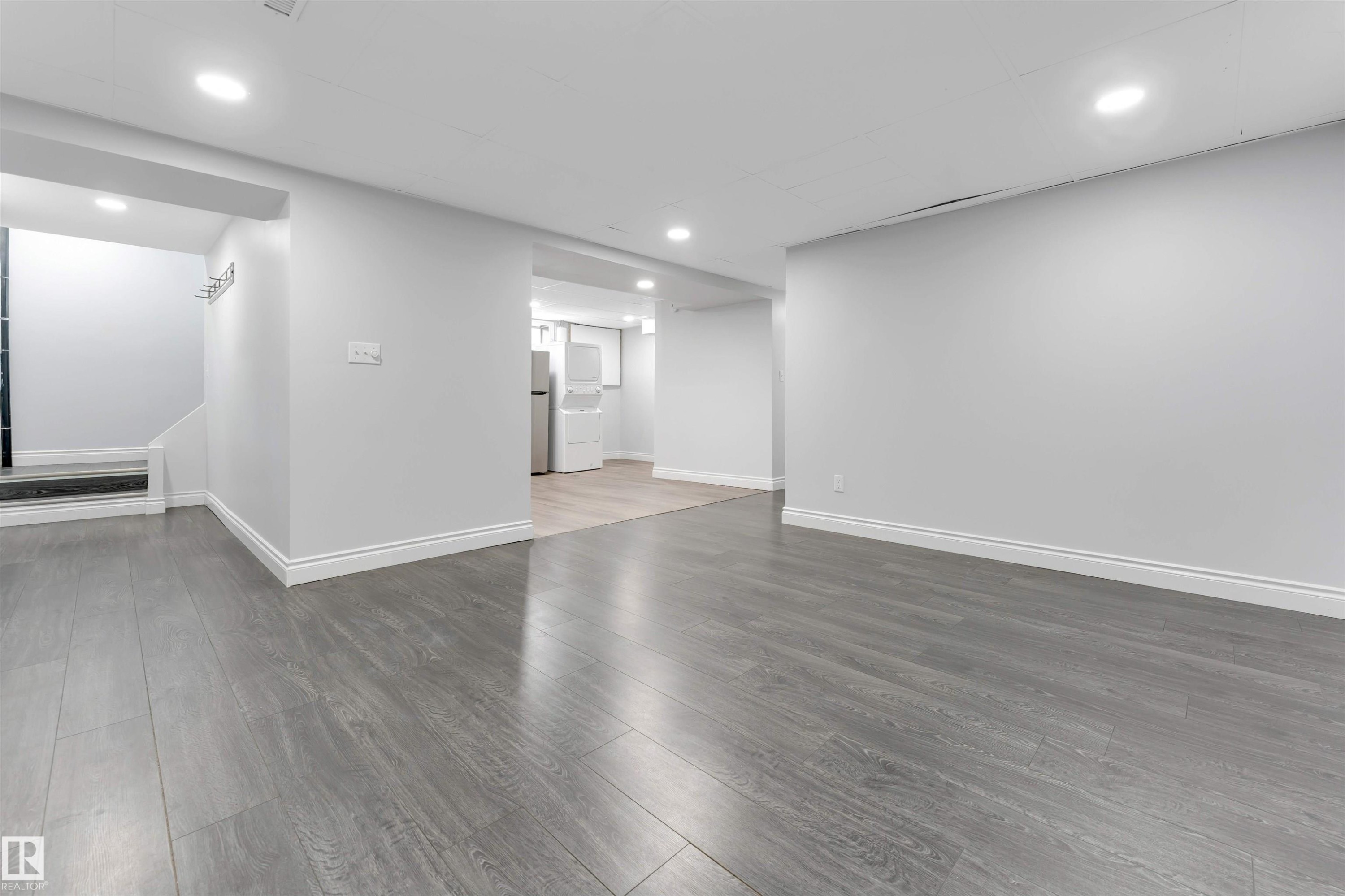 Spacious open-concept room featuring gray wood-finish flooring, recessed lighting, white baseboards, and painted walls - 7419 33 Avenue Nw, Edmonton, AB - Indoor Photo Showing Other Room