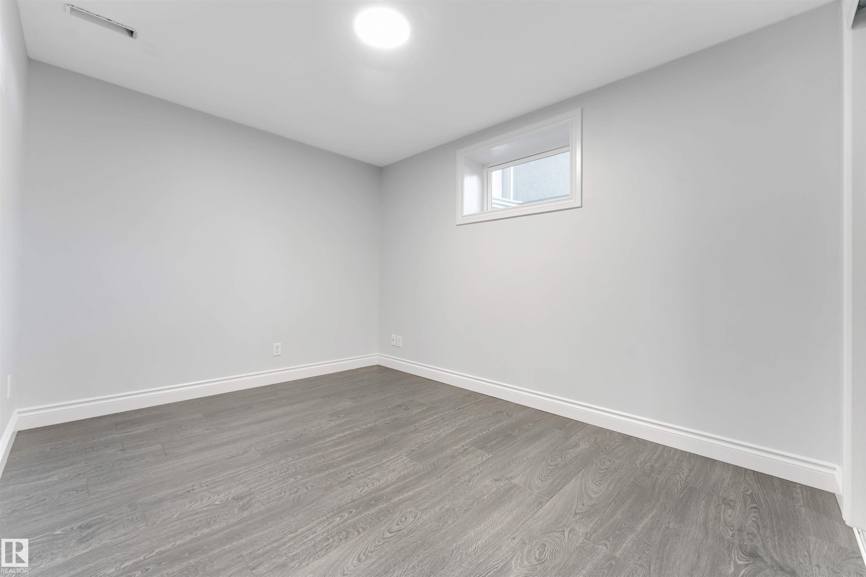 Room featuring light gray walls, wood-finish flooring, white baseboards, and a single window with white trim - 7419 33 Avenue Nw, Edmonton, AB - Indoor Photo Showing Other Room