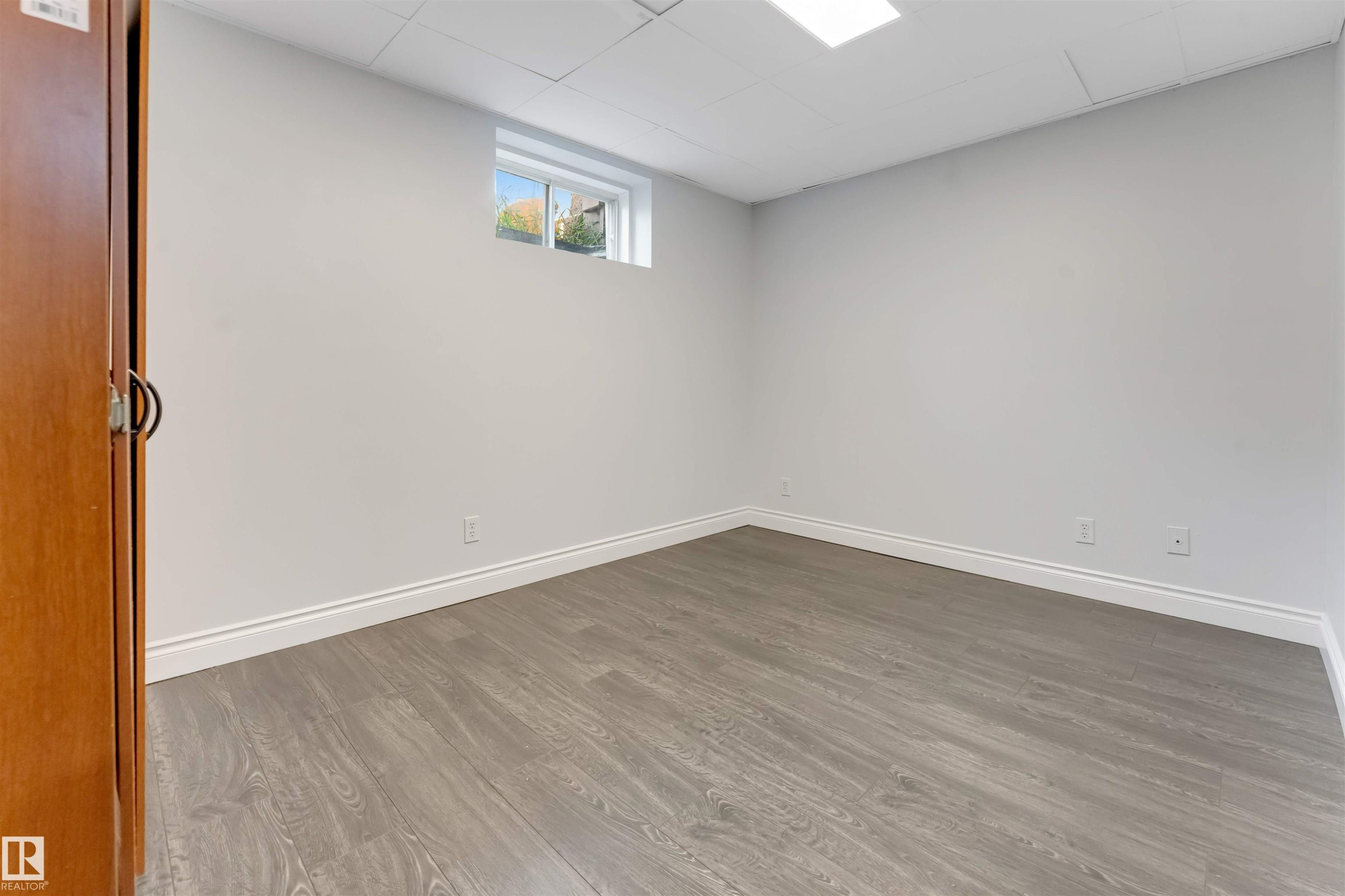 Room featuring light gray walls, wood-finish flooring, white baseboards, a single window, and a drop ceiling with a recessed light fixture - 7419 33 Avenue Nw, Edmonton, AB - Indoor Photo Showing Other Room